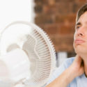Person feeling uncomfortable in warm weather, sitting near a fan, illustrating the need for effective air conditioning solutions in Melbourne.