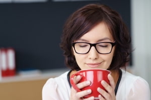 Woman enjoying a warm beverage from a red mug, emphasizing comfort and relaxation in a cozy indoor setting, relevant to indoor air quality and well-being.