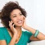 Smiling woman in a teal shirt talking on a smartphone, representing customer service and communication in HVAC consultations.