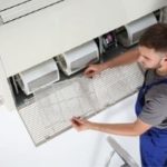 HVAC technician inspecting and replacing air filter in residential air conditioning unit, emphasizing importance of proper air quality maintenance for home health.