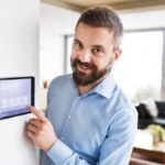 Man adjusting a digital thermostat in a modern home setting, highlighting HVAC technology and comfort solutions.