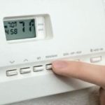 Digital thermostat with a finger adjusting the temperature settings, showcasing features relevant to HVAC maintenance and installation services.