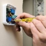 Hand adjusting wiring inside a digital thermostat, illustrating HVAC installation and maintenance services relevant to Mid-Florida Air Conditioning, Inc.
