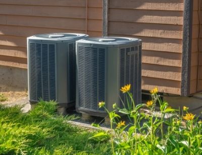 Air conditioning units outside a home, surrounded by green grass and flowers, illustrating HVAC systems for effective cooling and air quality control.