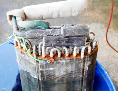 Corroded AC component with refrigerant lines, illustrating potential causes of refrigerant leaks and the importance of regular maintenance in HVAC systems.