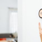 Hand adjusting a thermostat on a wall, emphasizing HVAC maintenance for optimal home temperature control.