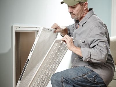 Man replacing an air filter in an HVAC system, emphasizing the importance of regular maintenance for energy efficiency and cost savings.