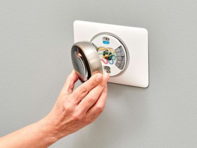 Hand installing a smart thermostat on a wall, showcasing wires and components, emphasizing energy efficiency and modern HVAC technology.
