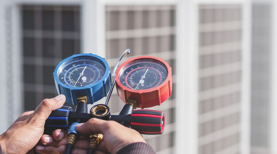 Man holding HVAC pressure gauges for air conditioning service, with a background of an outdoor AC unit, relevant to refrigerant leak detection and maintenance solutions in DeBary, FL.